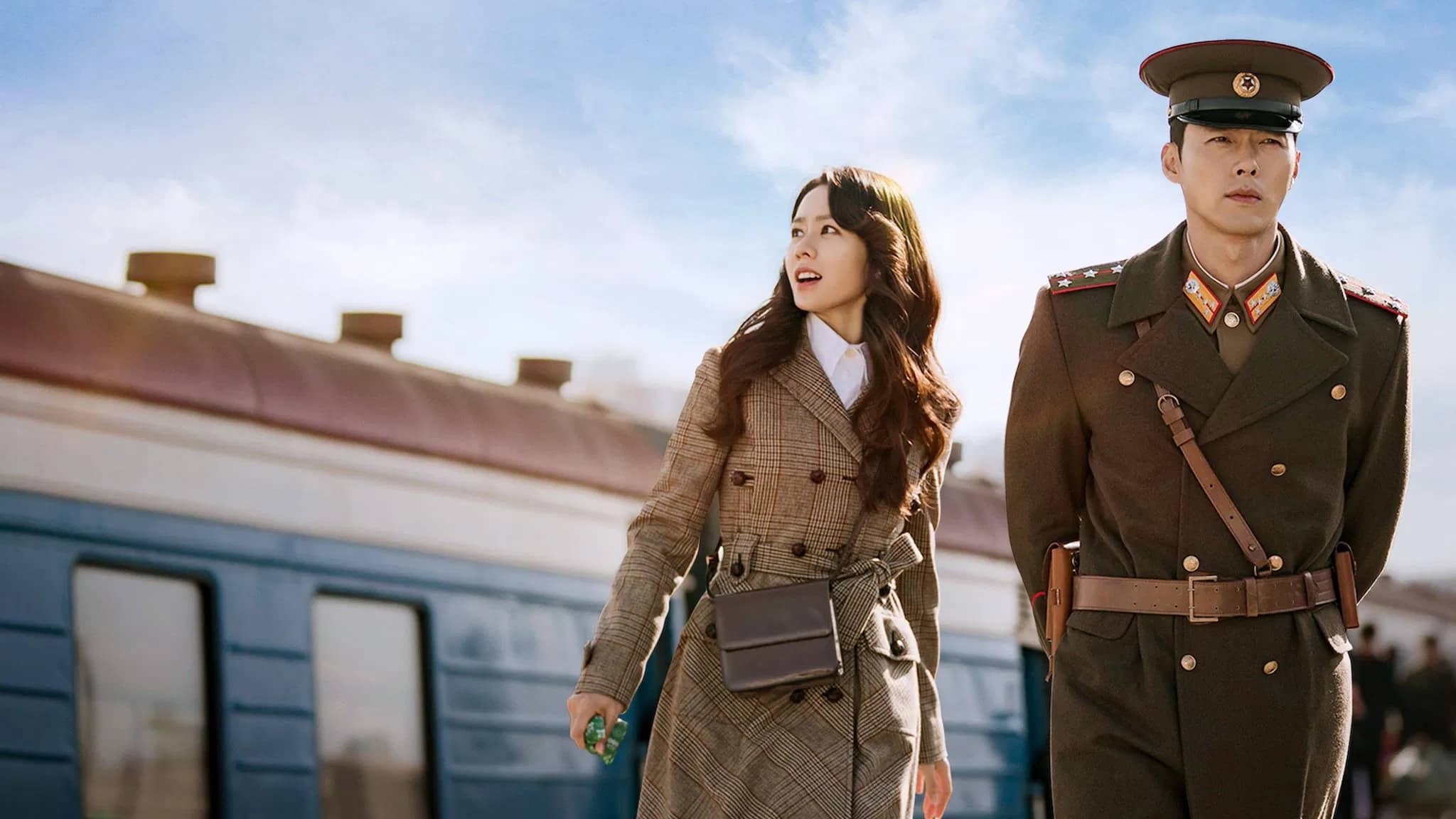 Yoon Se-ri looks around with curiosity as she takes in her unfamiliar surroundings, while Ri Jeong-hyeok walks ahead of her in his military uniform.